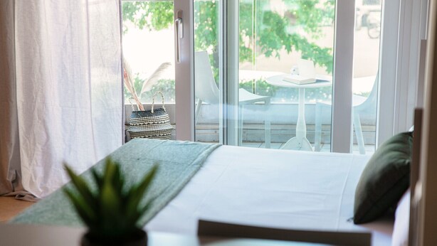Een slaapkamer met een bed, een potplant en uitzicht op een balkon met buitenmeubilair.
