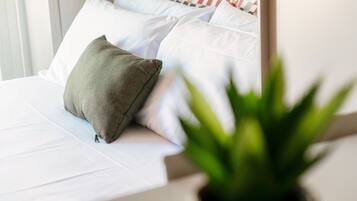Un letto con biancheria bianca e un cuscino verde, una pianta in vaso sullo sfondo e un cuscino decorato più lontano.