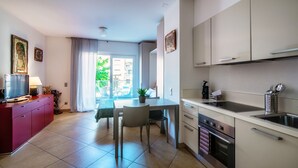 Een moderne keuken met witte kasten, een eethoek met een tafel en stoelen, en uitzicht naar buiten door een groot raam.