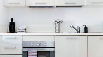 Una cucina moderna con mobili bianchi, una cappa in acciaio inossidabile, una macchina per il caffè, un bollitore, un set di utensili, un dispenser di sapone e un forno integrato.