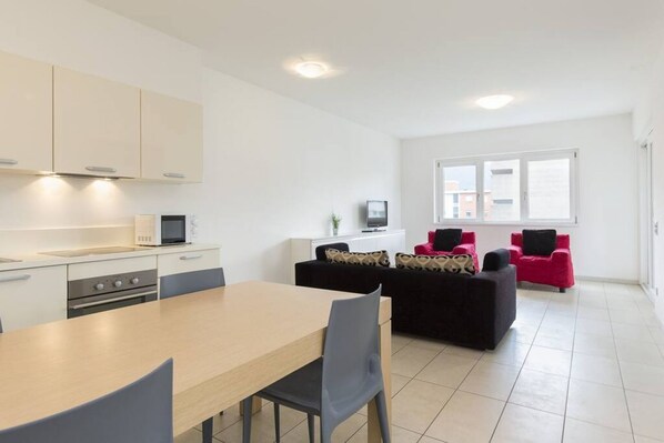 A modern kitchen with white cabinets, a dining table, and a black sofa in a bright living area with large windows. - Wonderful two-bedroom Apartment with a Bright Open Space in Lugano - PRESTIGE 34 (Lugano)