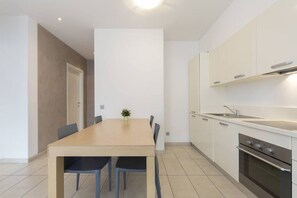 A modern kitchen with white cabinets, a wooden dining table, and a built-in oven. - Wonderful two-bedroom Apartment with a Bright Open Space in Lugano - PRESTIGE 34 (Lugano)