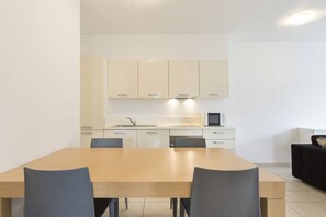A modern kitchen with white cabinets, a wooden dining table, and two chairs.