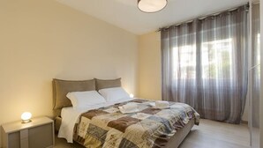 Un dormitorio con cama, mesita de noche, lámpara y ventana con cortinas.