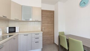 Cocina compacta con microondas, armarios y una puerta de madera. Hay una mesa de comedor con sillas y un reloj de pared.