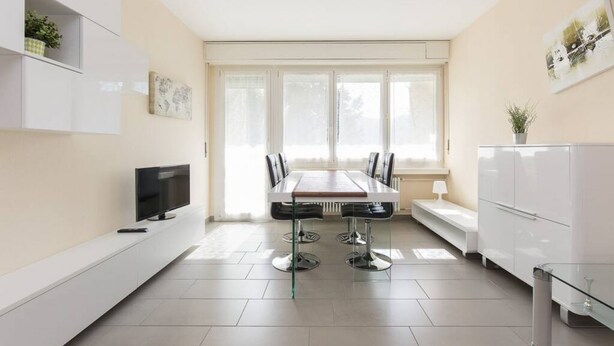 Una cocina moderna con una mesa, sillas, televisor y armarios empotrados.
