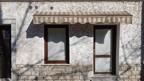 Fachada de edificio con dos ventanas, base de piedra y techo de metal.