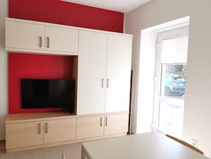A room with a white wardrobe, a red accent wall, and a large window with a view of a blue car outside. - Cube Studio By The River (Ljubljana)