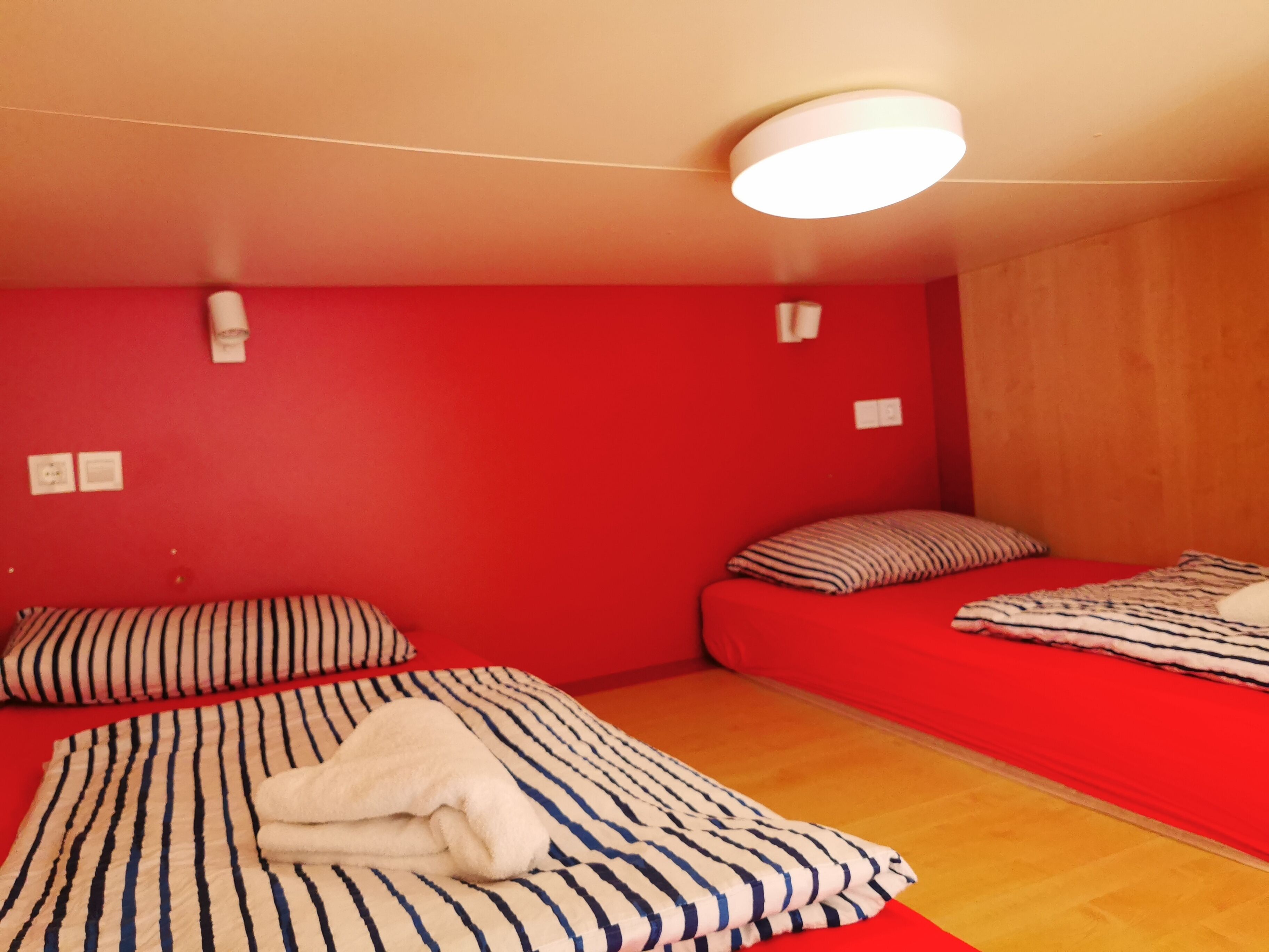 A room with two beds, red walls, and a wooden floor.