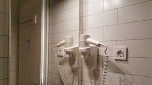 Un baño con dos secadores de pelo montados en la pared, un lavamanos blanco y un espejo.