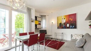 A modern living room with a glass dining table, red chairs, a grey sofa, and a red rug.