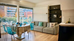 A modern living room with a dining area, a sofa with cushions, and a bookshelf.