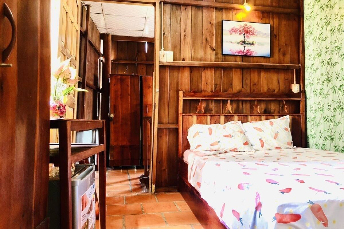 A wooden room with a bed, a shelf with decorative items, and a door leading to another room.