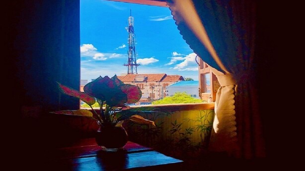 A room with a window overlooking a building with a tall communication tower. - HOANG BAO VY (Phu Quoc)