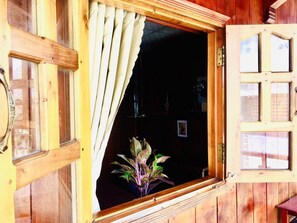 A wooden-framed window with a curtain, a potted plant inside, and a door with glass panels. - HOANG BAO VY (Phu Quoc)