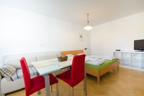 Une pièce moderne et bien éclairée, avec un lit en bois, un canapé blanc, un fauteuil rouge et une petite table sur laquelle se trouve un panier.