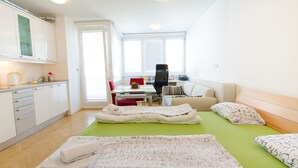 A bright, modern room with a kitchenette, a dining area, and a bed with green bedding. - City centre studio with a balcony (Ljubljana)