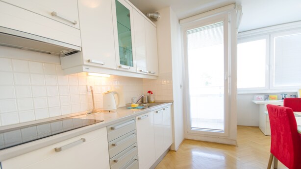 A modern kitchen with white cabinets, a built-in oven, and a window with blinds. - City centre studio with a balcony (Ljubljana)