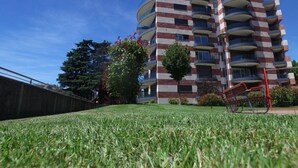 A multi-story residential building with balconies, a well-maintained lawn, and a clear blue sky.
