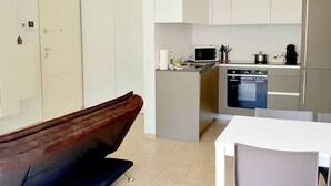 A compact kitchen with a microwave, stove, and dishwasher. A brown chair is visible in the foreground.