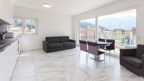 A modern apartment with a kitchen, dining area, and large windows offering a mountain view. - Apartment two steps from the Exhibition Center of Lugano - ROGGIA 17 (Lugano)