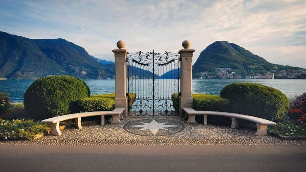 A gated entrance with a star-patterned pavement, surrounded by neatly trimmed bushes and a bench. - Apartment two steps from the Exhibition Center of Lugano - ROGGIA 17 (Lugano)