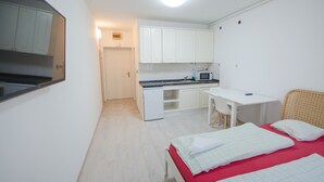 Ein gemütlicher Raum mit einer Küchenzeile, einem Bett mit roter Matratze und einem kleinen Schreibtisch.
