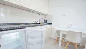 Eine moderne Küche mit weißen Schränken, einer eingebauten Mikrowelle, einem Kühlschrank mit durchsichtigen Regalen sowie einem Essbereich mit weißem Tisch und Stühlen.