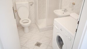 Ein Badezimmer mit Toilette, Dusche, Waschbecken und Waschmaschine.