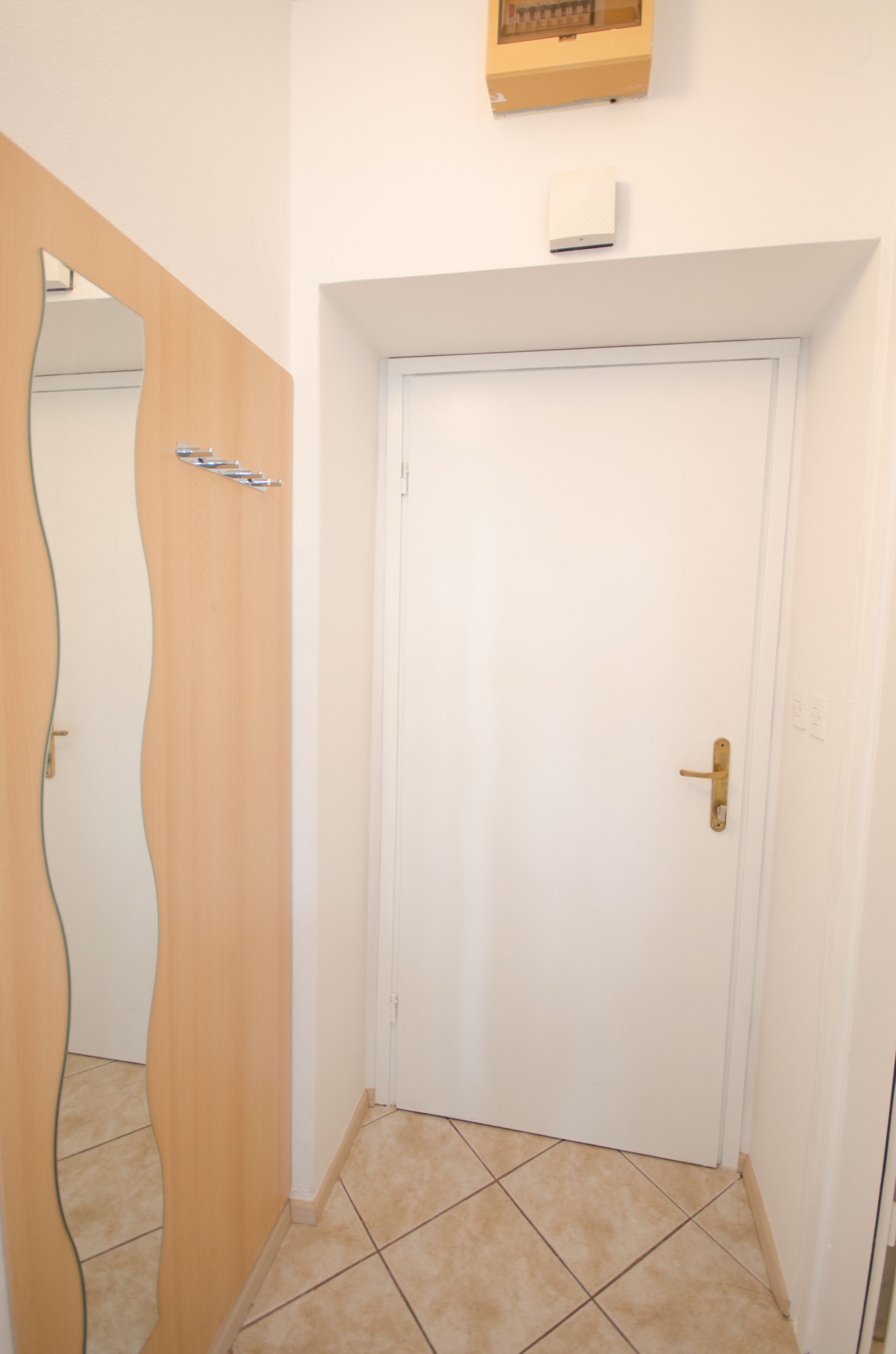 En gang med en hvid dør, en trædørramme og et flisegulv.