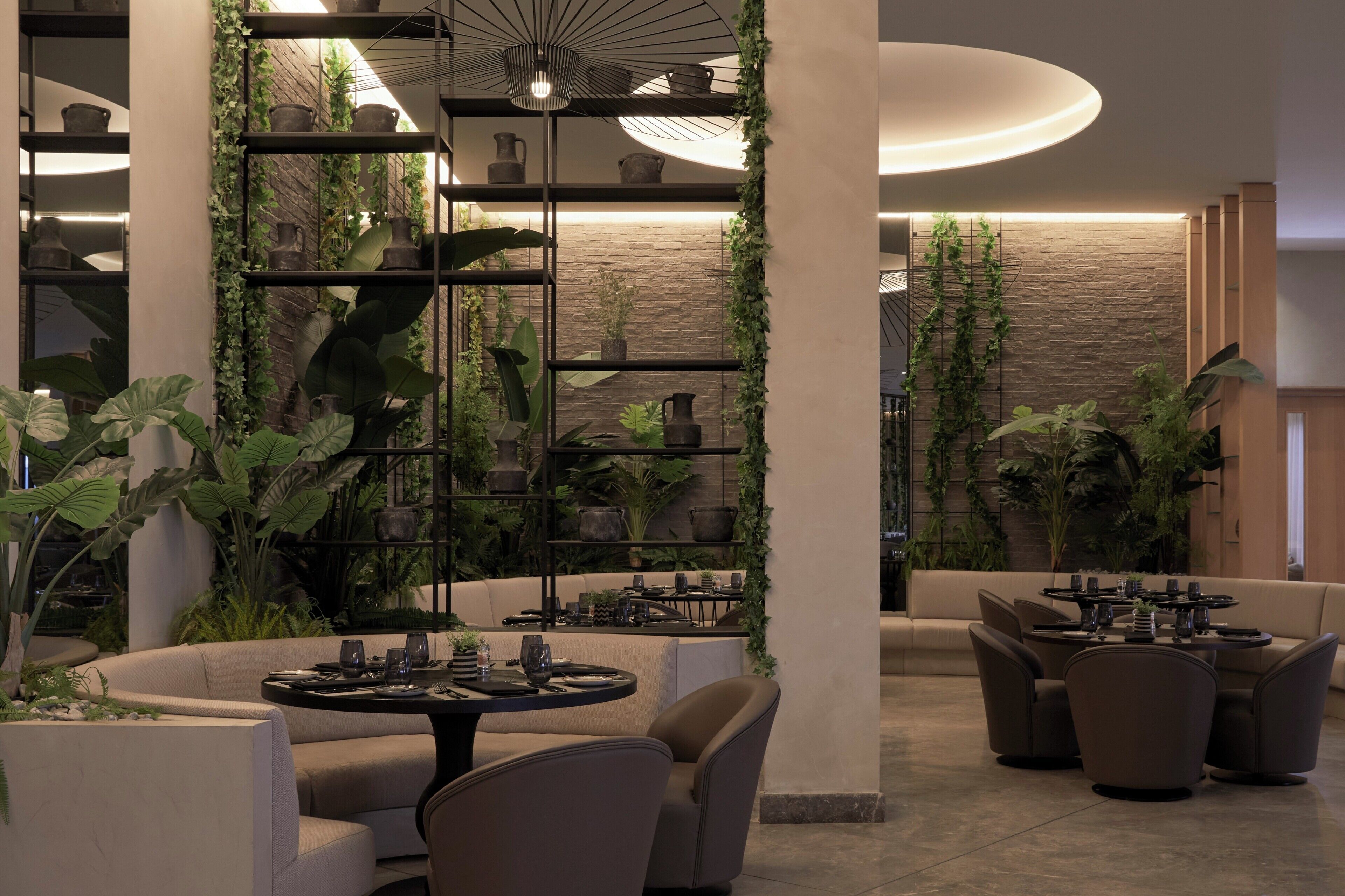 Un interior moderno con zona de comedor, sofás y una pared decorada con plantas y cerámica.