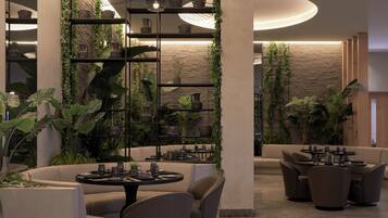 Un interior moderno con zona de comedor, sofás y una pared decorada con plantas y cerámica.