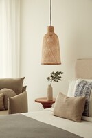 A bedroom with a bed, pillows, a bedside table, a vase with a plant, and a hanging light fixture.