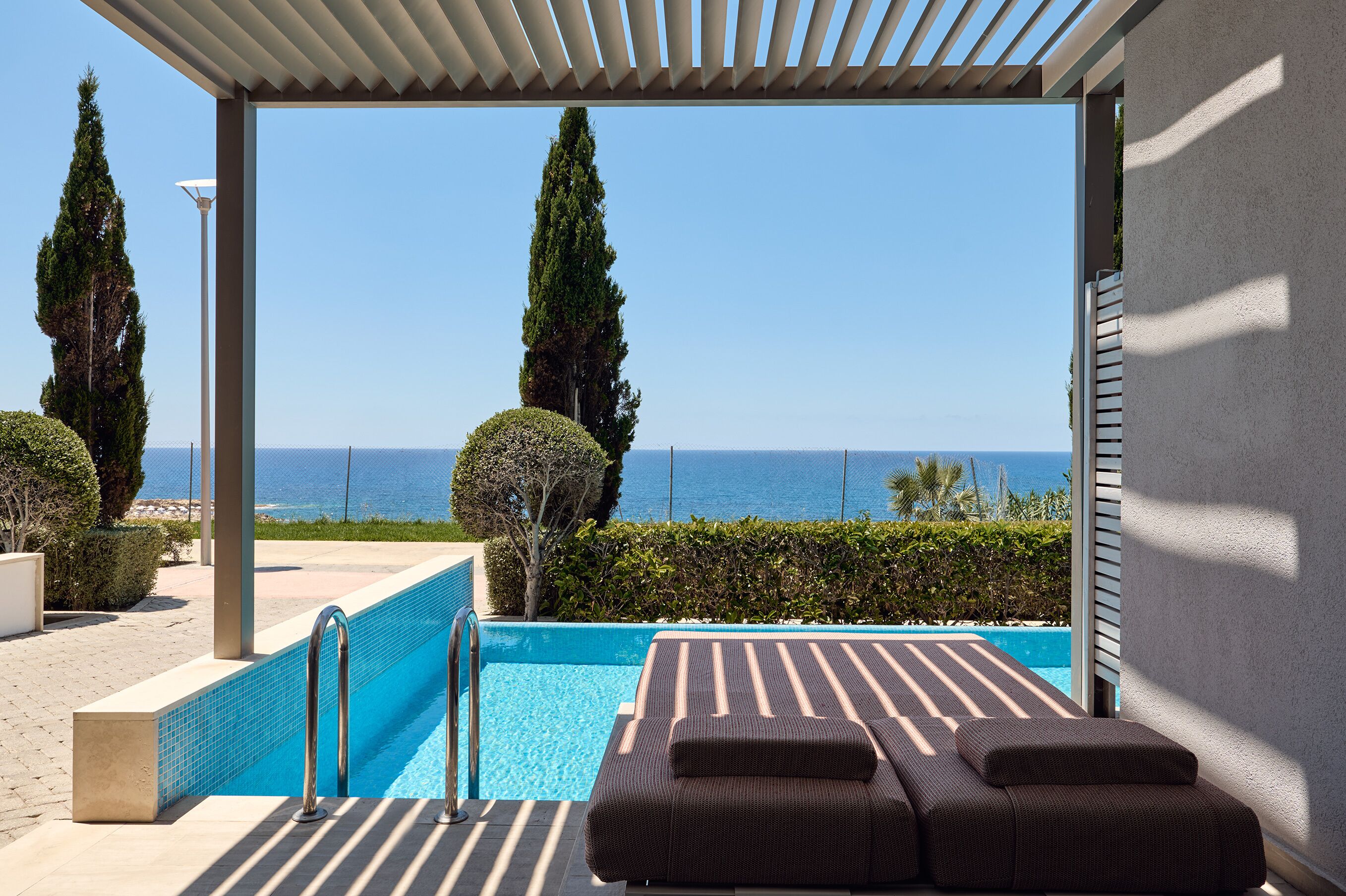 Uma área à beira da piscina com vista para o mar, um espaço coberto para sentar e um céu limpo.
