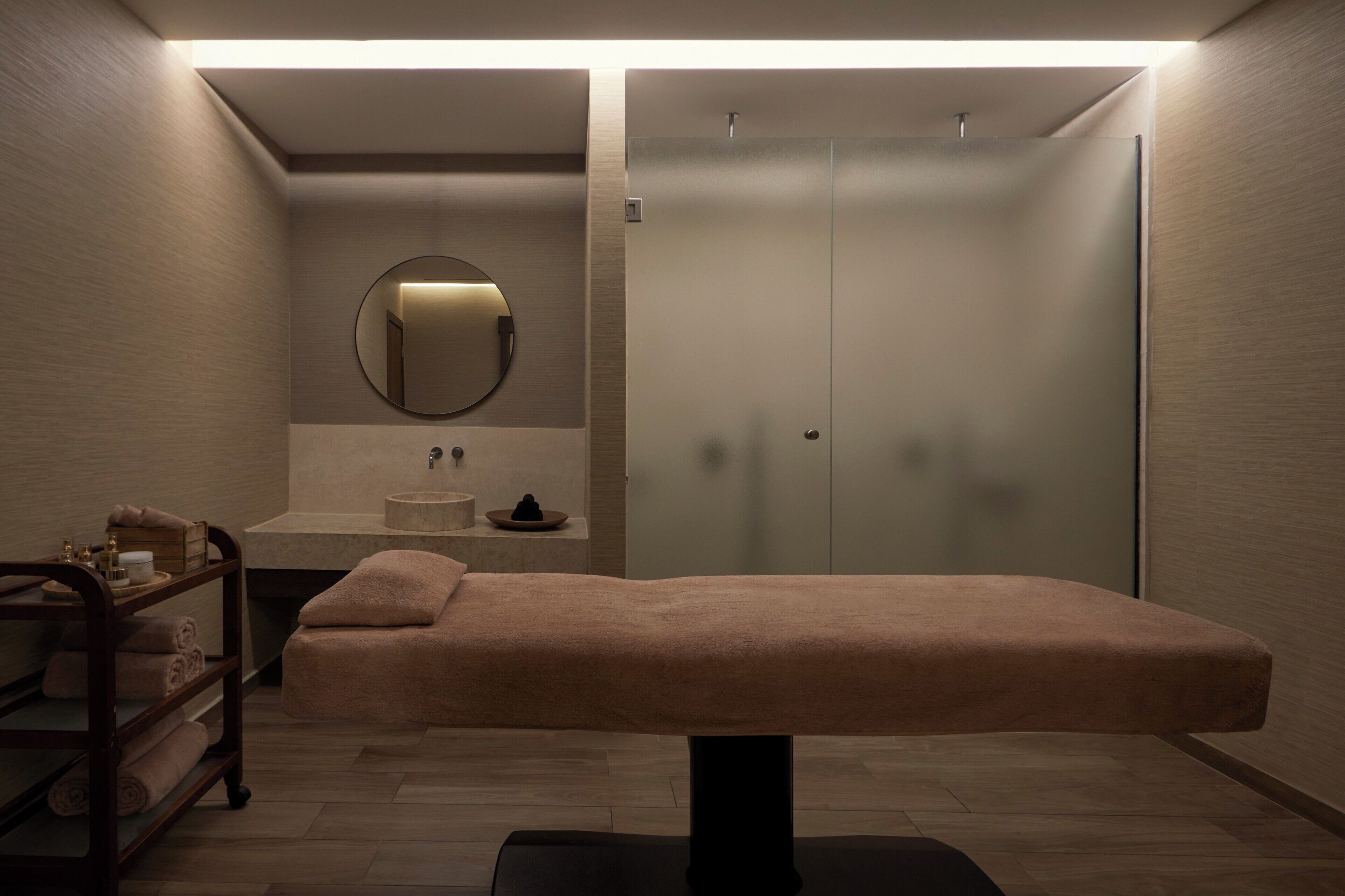 Et moderne spa-rum med en massagestol, håndvask, spejl og en brusekabine i glas.