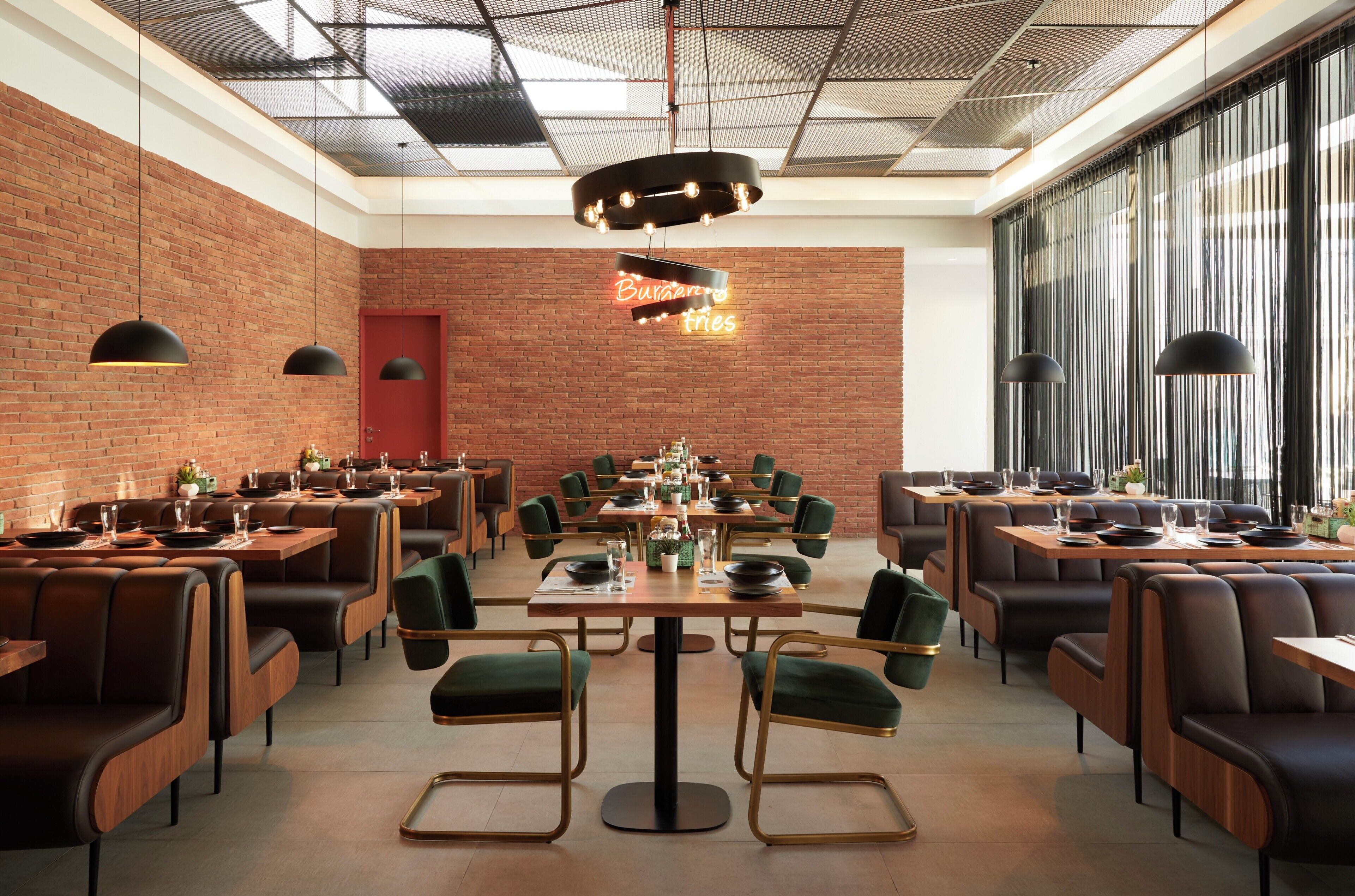 A restaurant with brick walls, multiple dining tables, and green upholstered chairs.