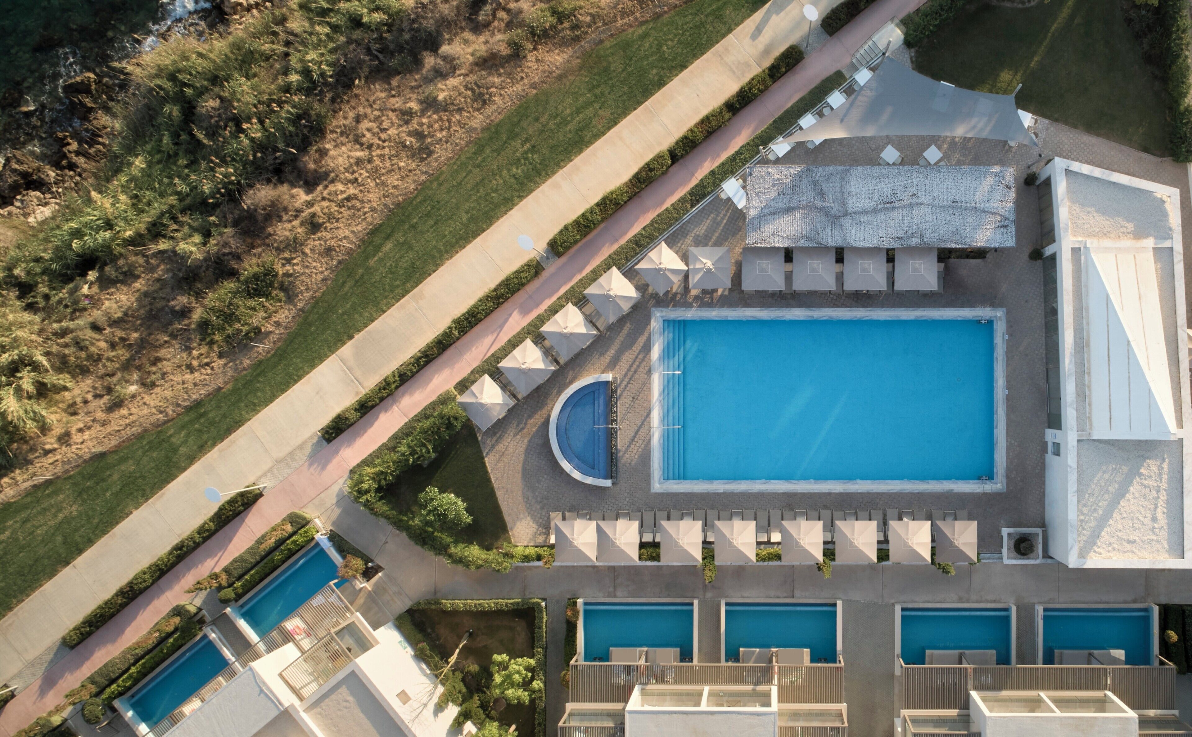 An aerial view of a resort with multiple swimming pools, a large central pool, and a landscaped area with pathways and seating.