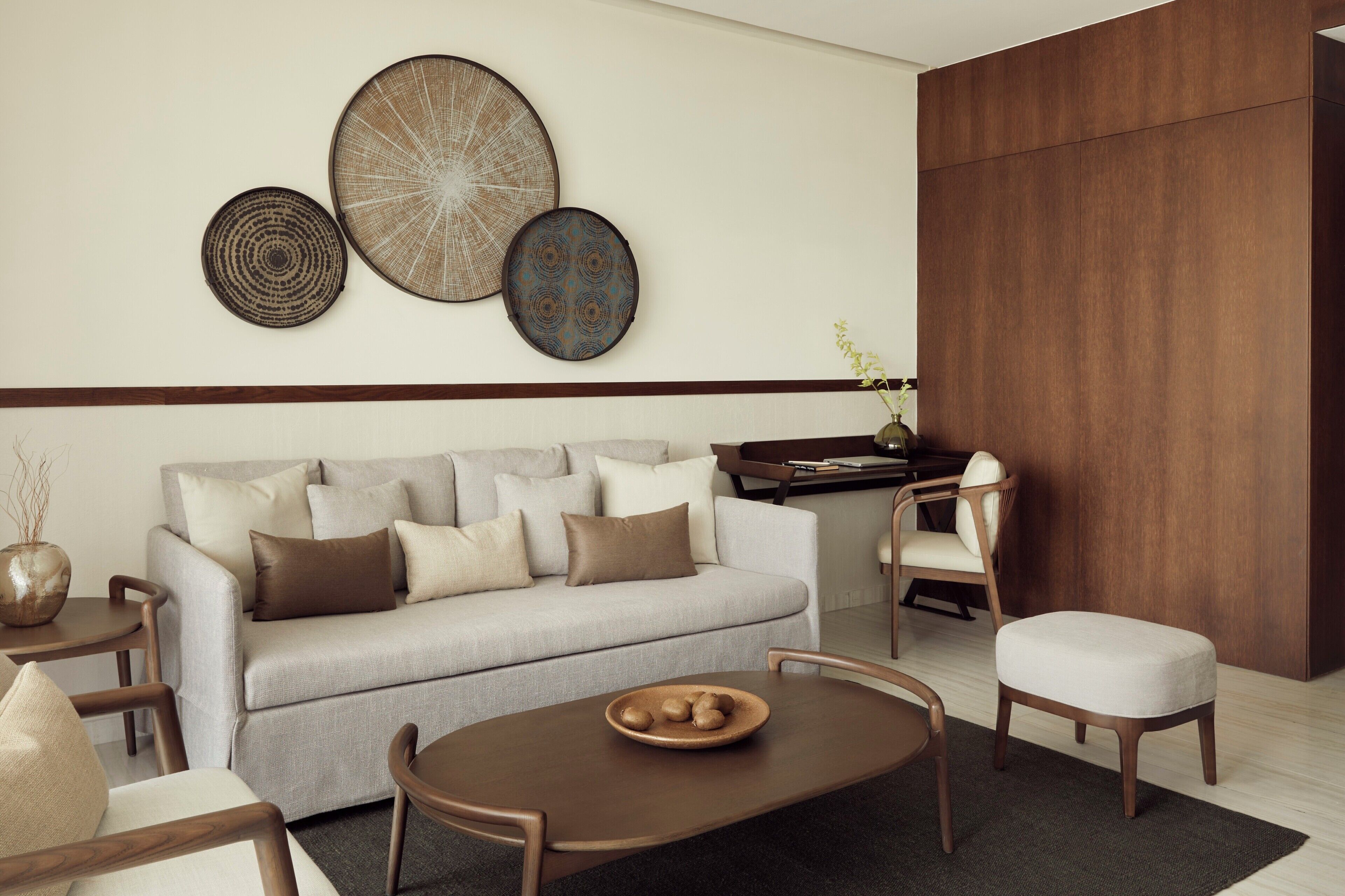 A modern living room with a sofa, coffee table, and chairs. There are decorative wall pieces above the sofa.