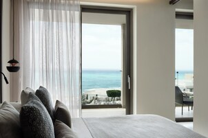 A bedroom with a bed, a window with sheer curtains, and a view of the sea.