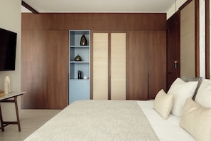 A bedroom with a bed, a nightstand, a shelf with decorative items, and a wardrobe. - Mare Paphos (Kissonerga)