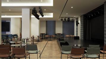A spacious conference room with a stage, multiple tables, and chairs arranged for meetings.