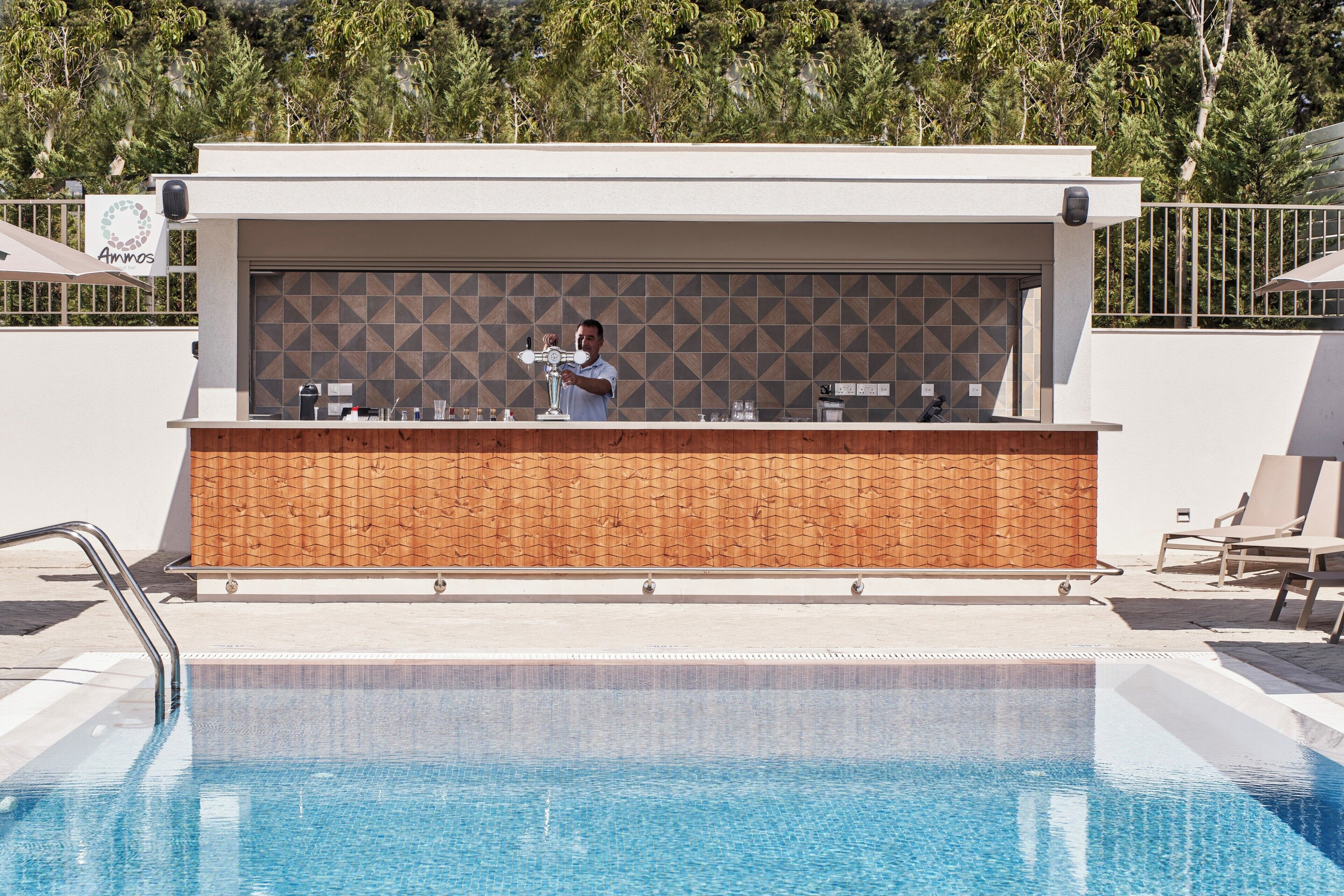 Un bar junto a la piscina con un coctelero, un salpicadero de azulejos y sillones de descanso.