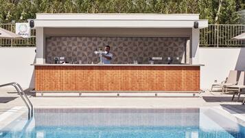 Un bar junto a la piscina con un coctelero, un salpicadero de azulejos y sillones de descanso.