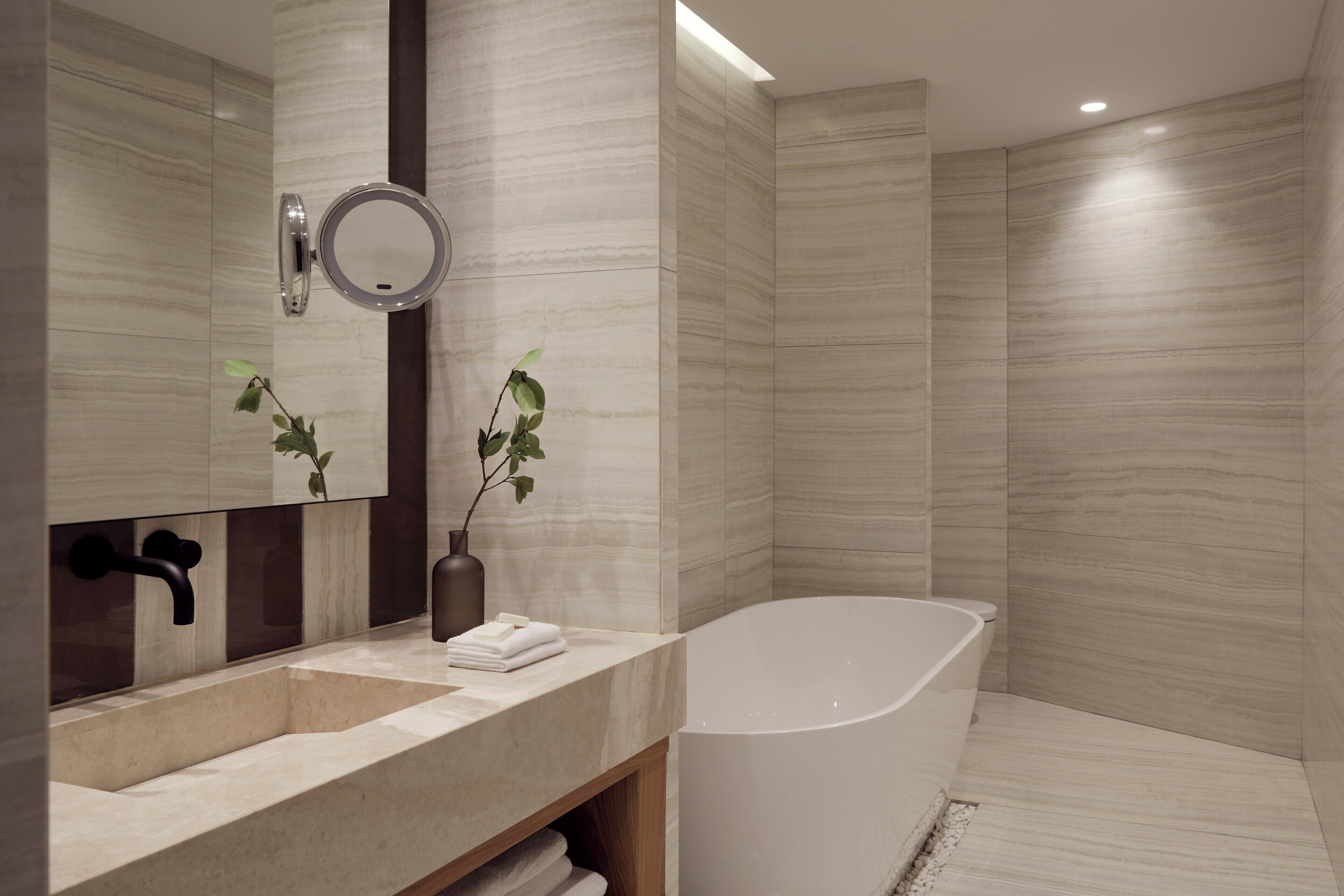 Un baño moderno con una bañera independiente, un tocador con espejo y dos plantas en macetas.