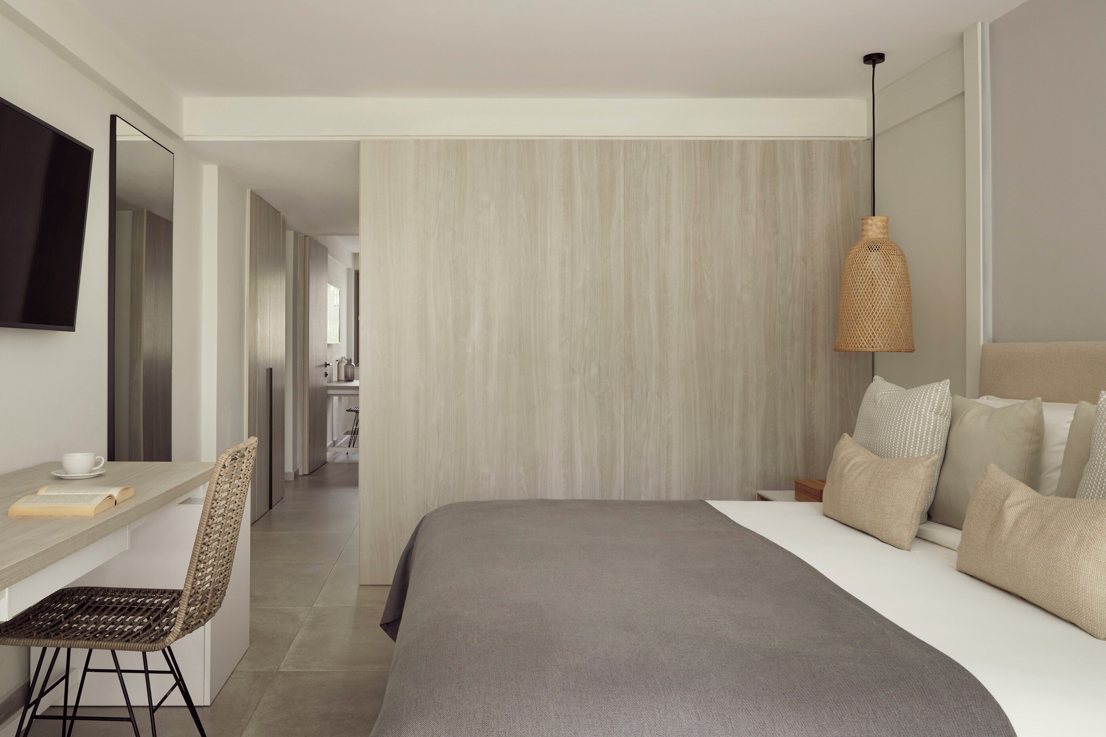 Une chambre d’hôtel moderne équipée d’un lit, d’un bureau, d’une chaise, d’une télévision et d’un luminaire suspendu.