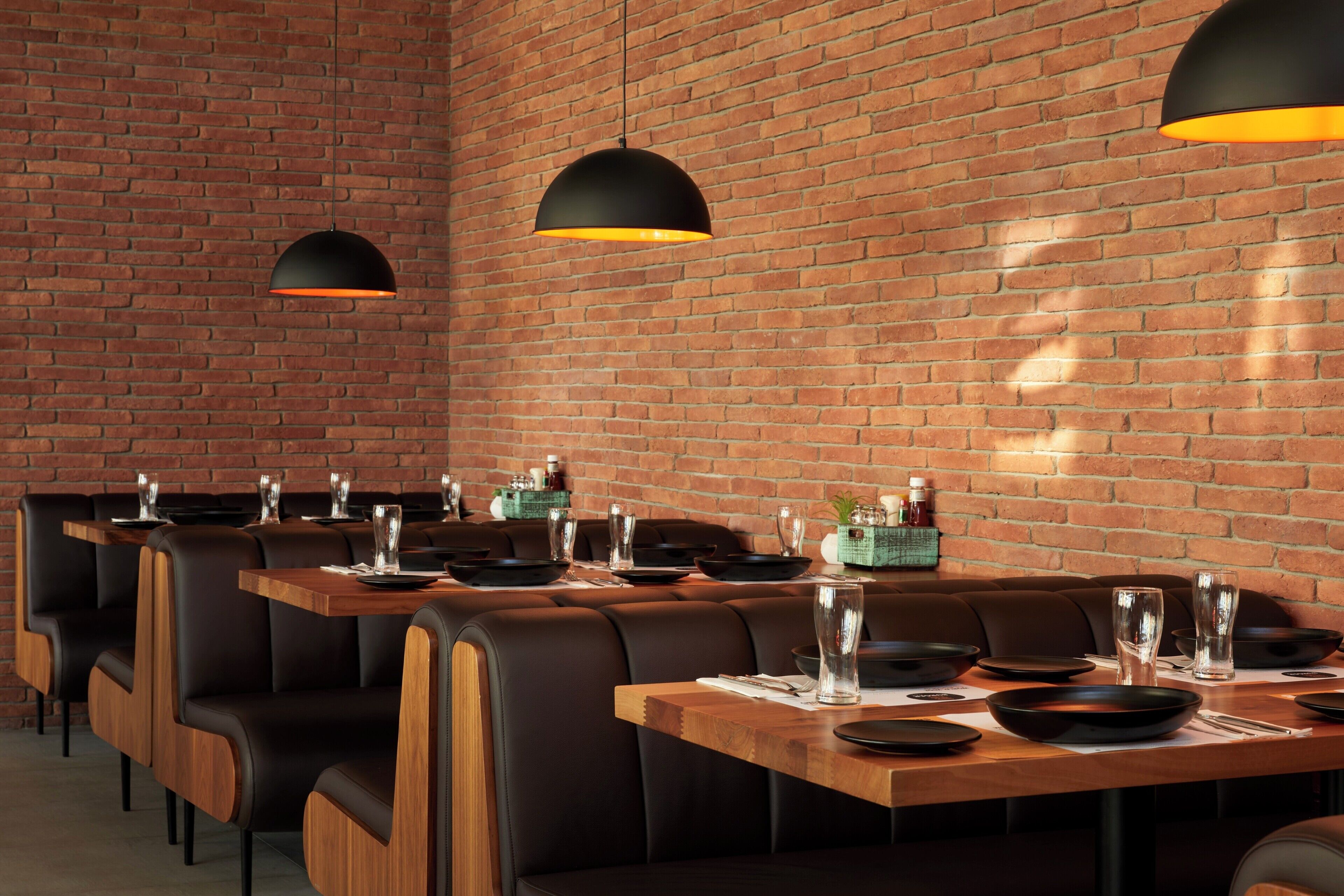 Interior de restaurante com paredes de tijolo, assentos de couro preto e mesas de madeira.