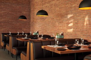 Interior de restaurante con paredes de ladrillo, asientos tipo banqueta de cuero negro y mesas de madera.