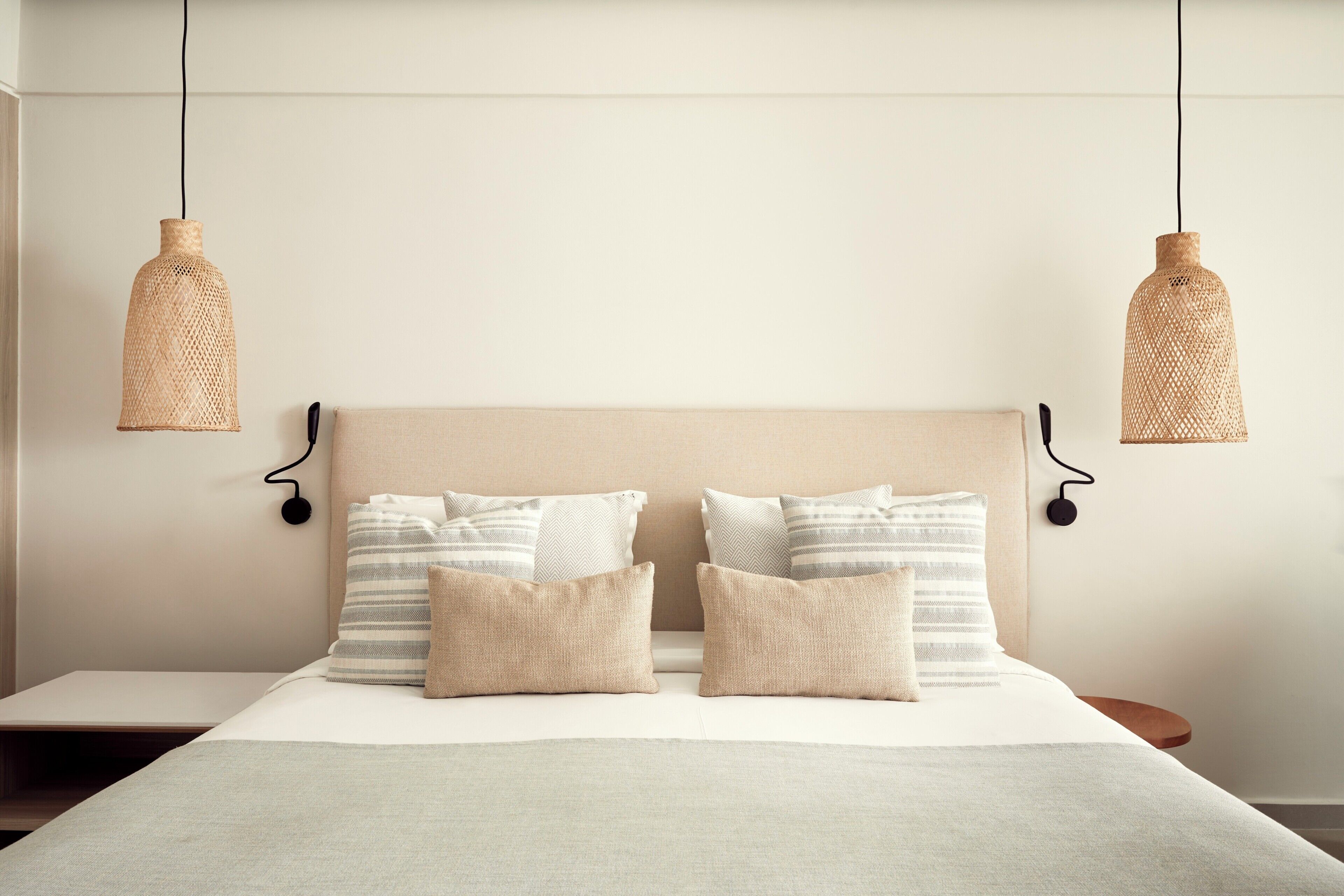 A neatly made bed with a plain headboard, two bedside lamps, and a bedside table with a lamp.