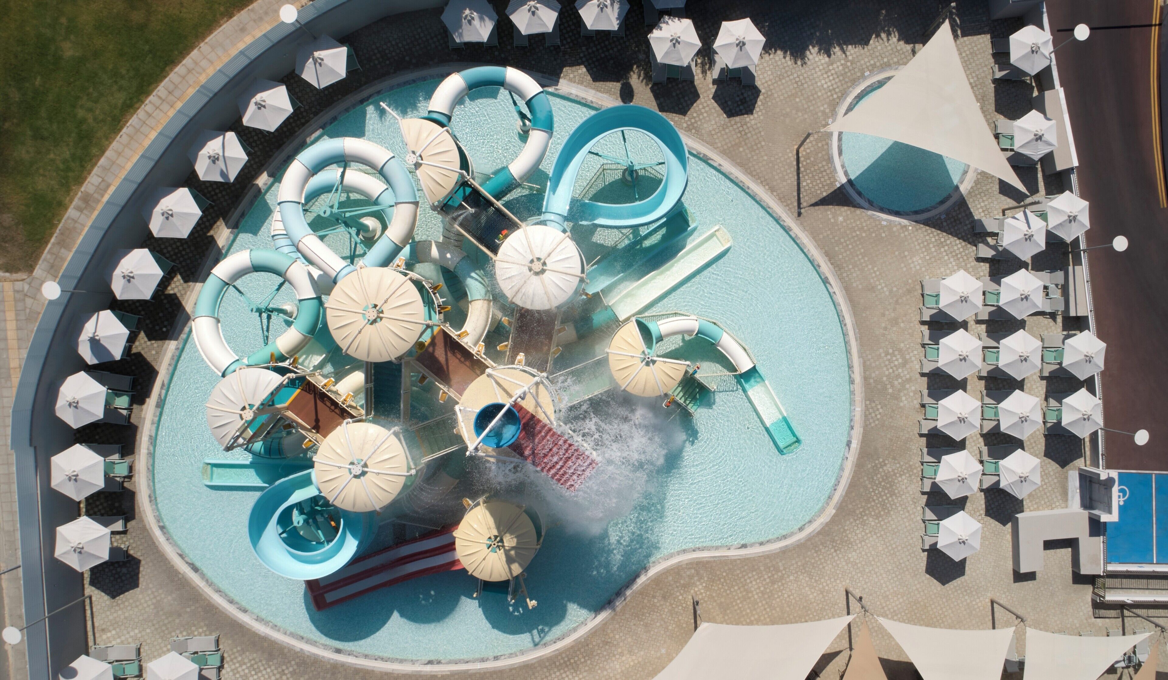 An aerial view of a water park with multiple slides and pools, surrounded by umbrellas and seating areas.