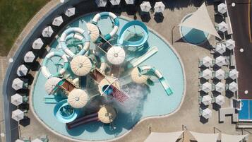 An aerial view of a water park with multiple slides and pools, surrounded by umbrellas and seating areas.